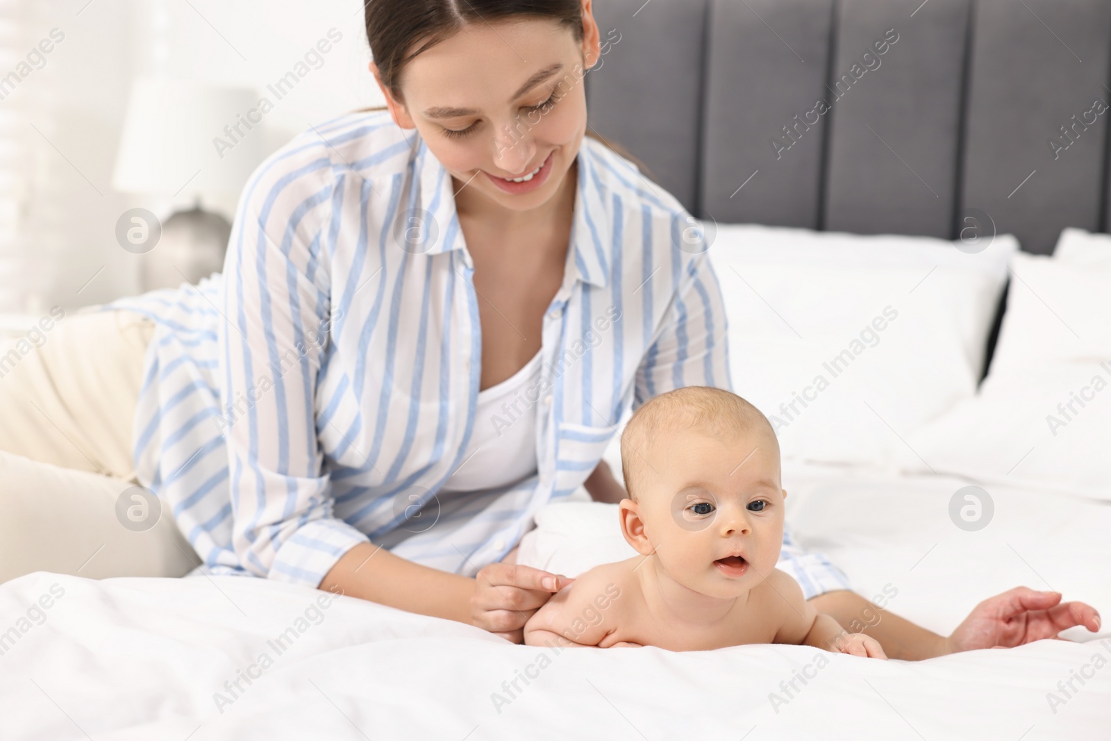 Photo of Happy young woman applying body cream onto baby`s skin on bed