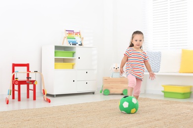 Photo of Cute little girl playing with ball at home, space for text. Soft toy