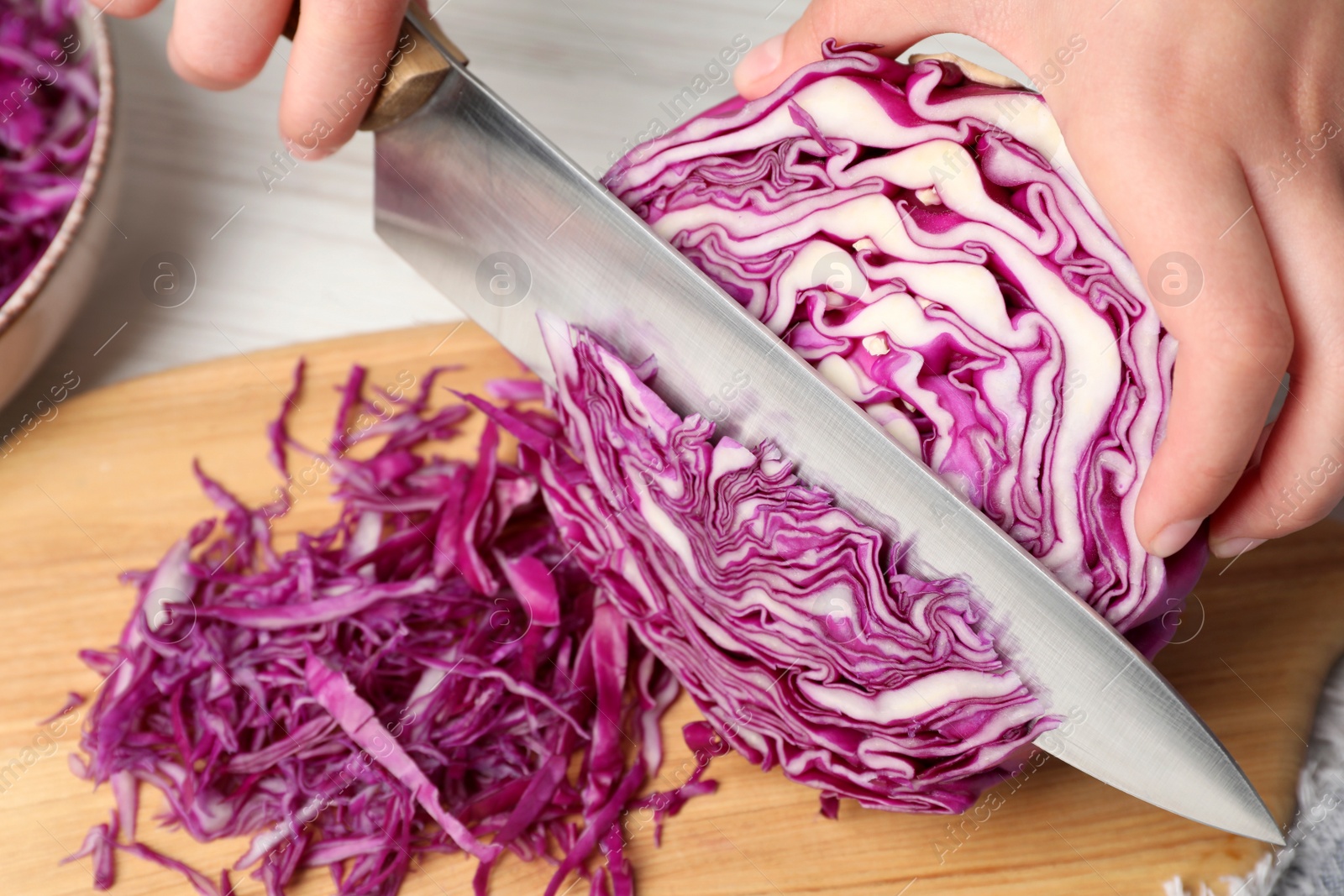 Photo of Woman cutting fresh red cabbage at white wooden table, closeup