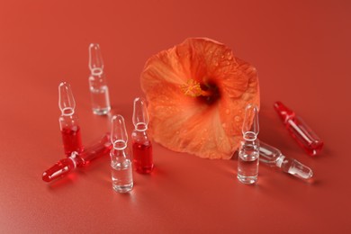 Skincare ampoules and hibiscus flower on coral background