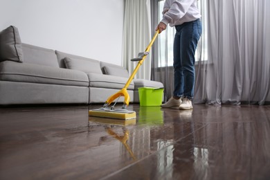 Woman cleaning parquet floor with mop indoors, closeup