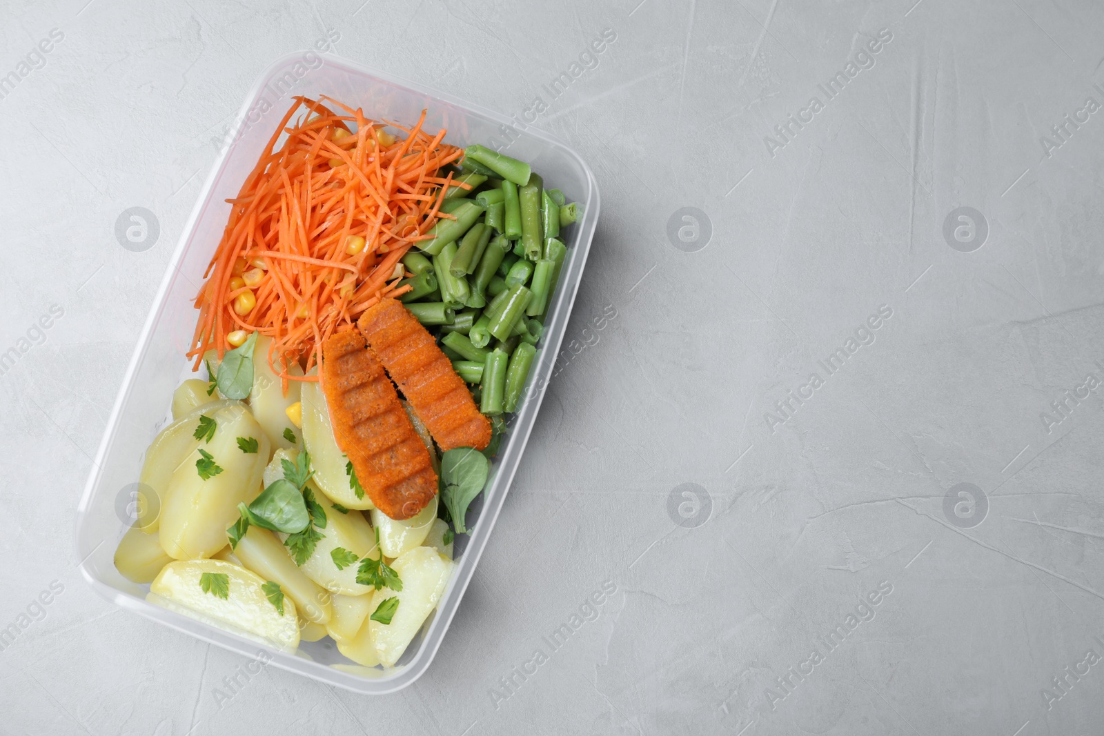 Photo of Tasty potatoes with cutlets and vegetables in plastic container on light table, top view. Space for text