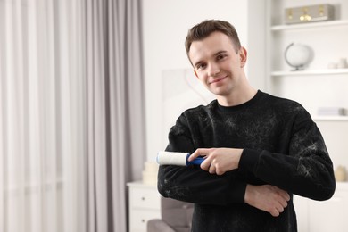 Pet shedding. Man with lint roller removing dog's hair from sweater at home. Space for text