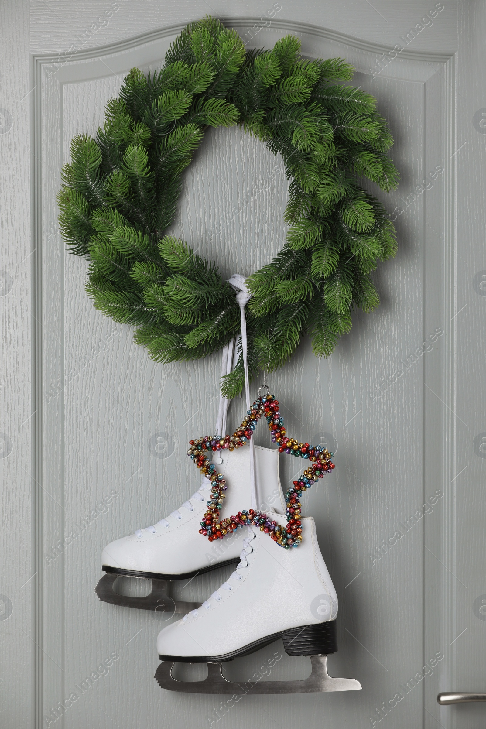 Photo of Pair of ice skates and Christmas wreath hanging on grey wooden door