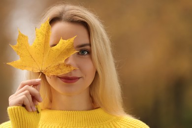 Photo of Portrait of beautiful woman covering eye with autumn leaf outdoors. Space for text