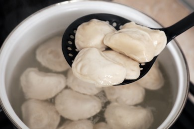 Photo of Dumplings (varenyky) with tasty filling on skimmer over pot, closeup