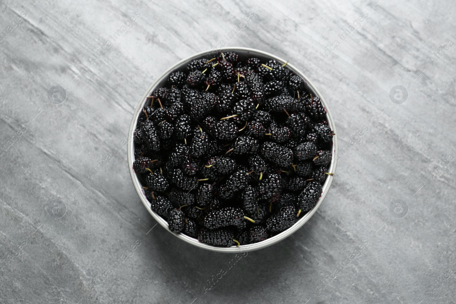 Photo of Bowl of delicious ripe black mulberries on grey table, top view