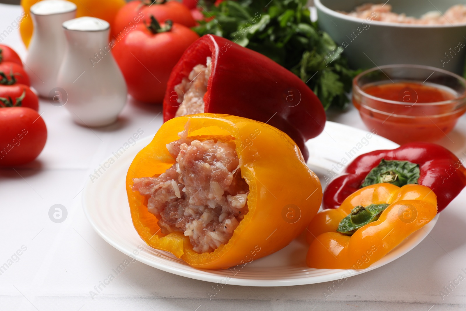 Photo of Raw stuffed peppers, ground meat and ingredients on white table, closeup