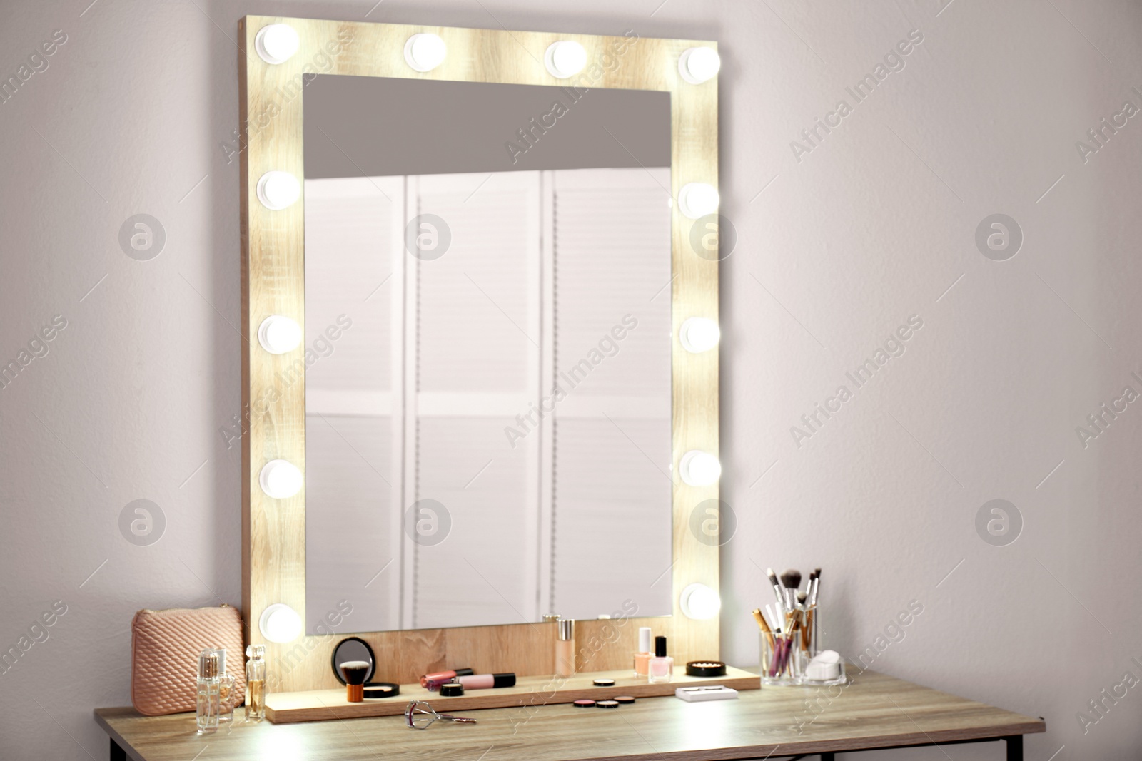 Photo of Table with makeup products and mirror near white wall. Dressing room interior