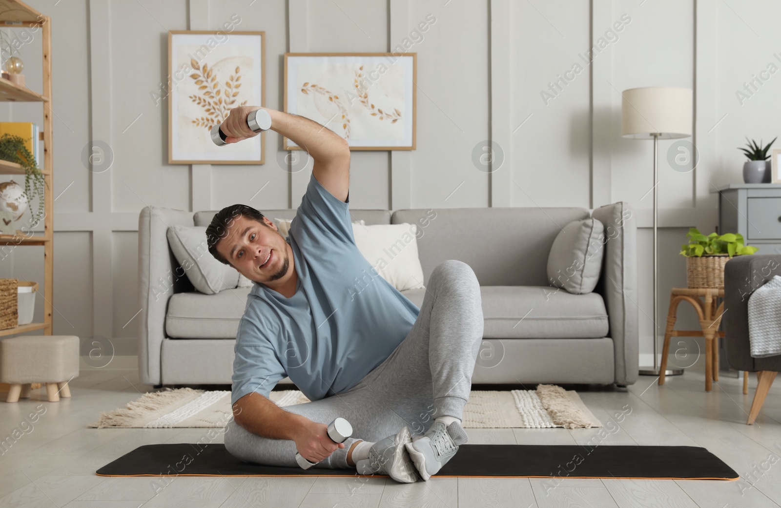 Photo of Overweight man doing exercise with dumbbells on mat at home