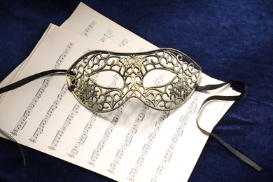 Photo of Elegant face mask and music sheets on blue fabric. Theatrical performance