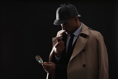 Photo of Old fashioned detective with smoking pipe and magnifying glass on dark background
