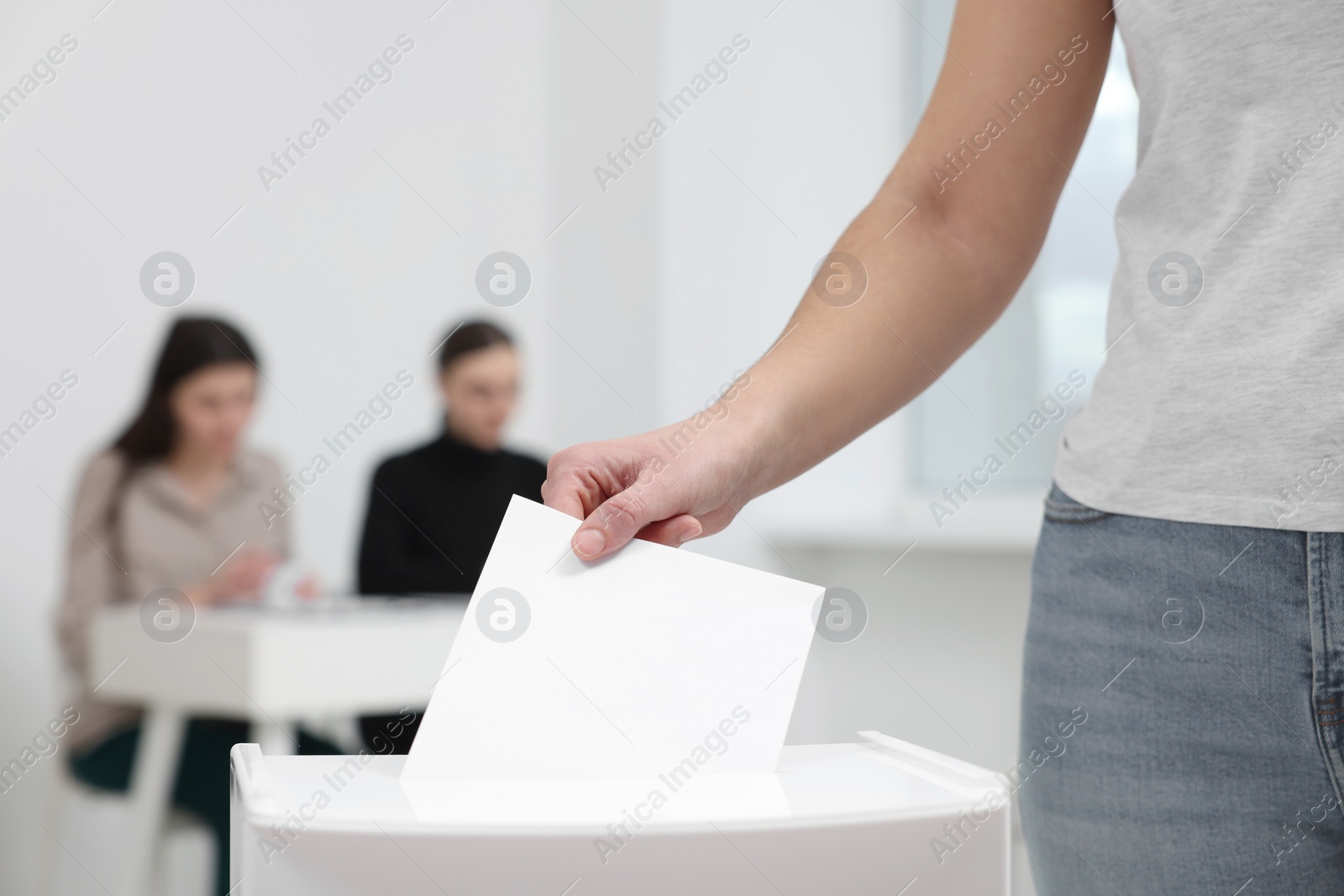 Photo of Woman putting her vote into ballot box on blurred background, closeup