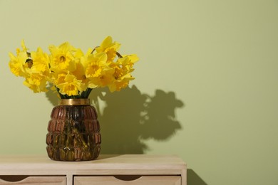 Beautiful daffodils in vase on table near light green wall, space for text