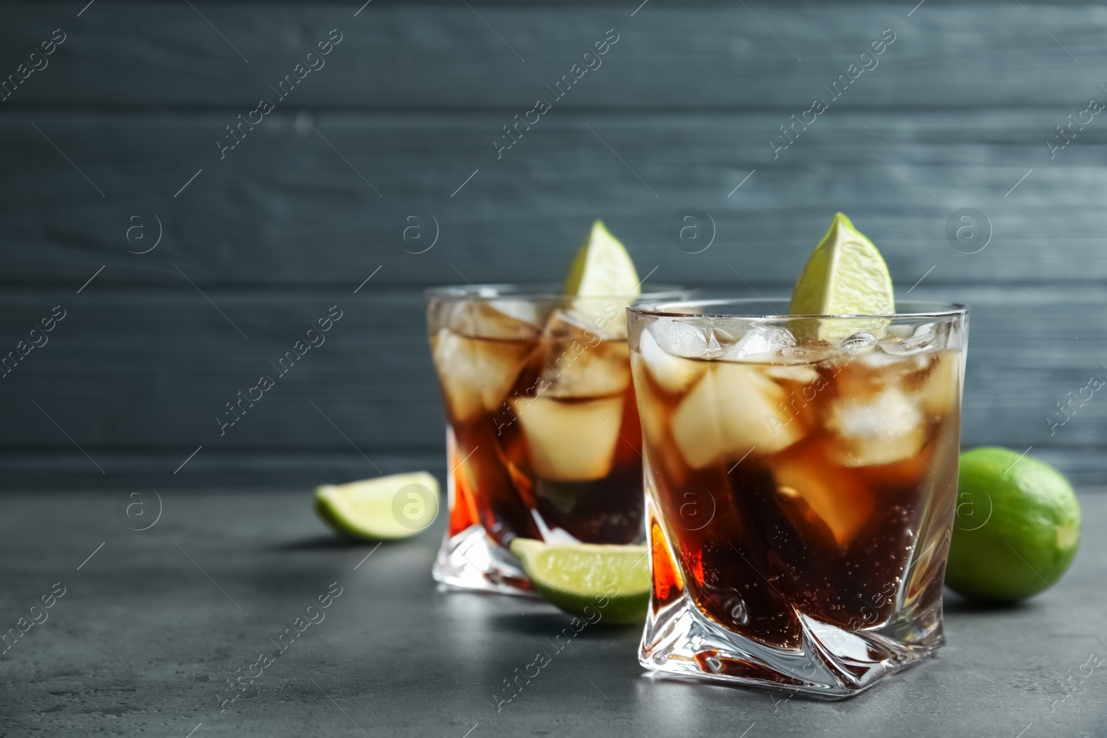 Photo of Glasses of cocktail with cola, ice and cut lime on table. Space for text