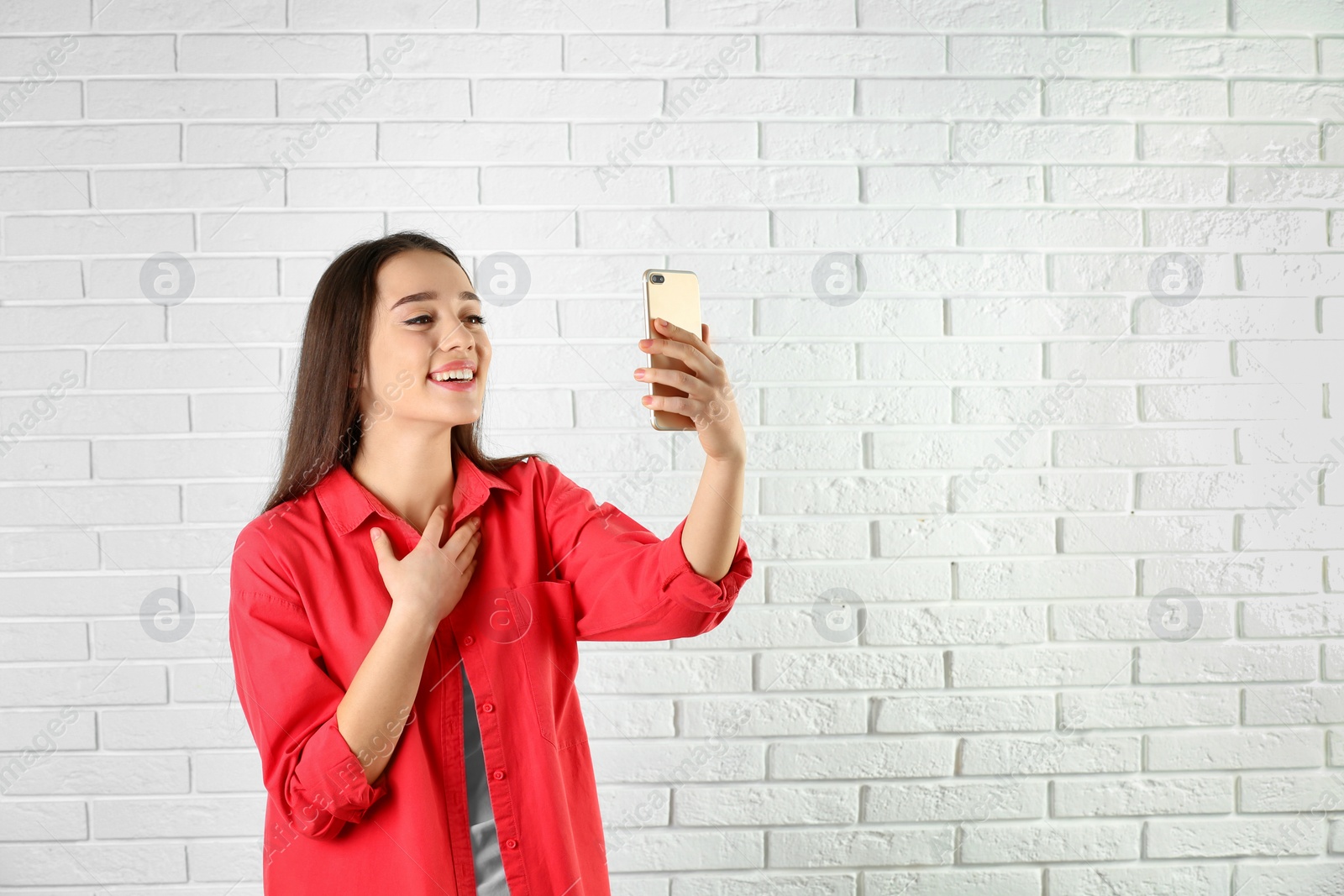 Photo of Woman using mobile phone for video chat against brick wall. Space for text