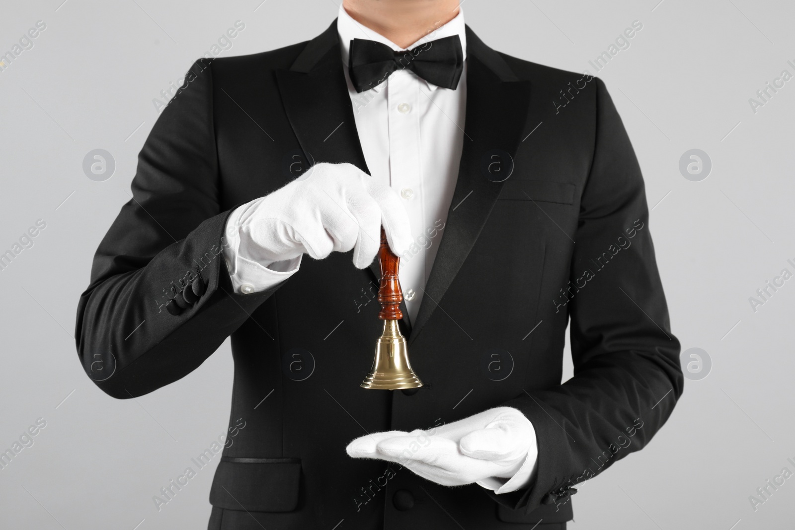 Photo of Butler holding hand bell on grey background, closeup