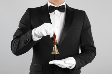 Photo of Butler holding hand bell on grey background, closeup