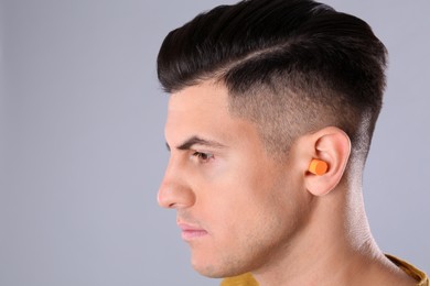 Man wearing foam ear plug on grey background, closeup