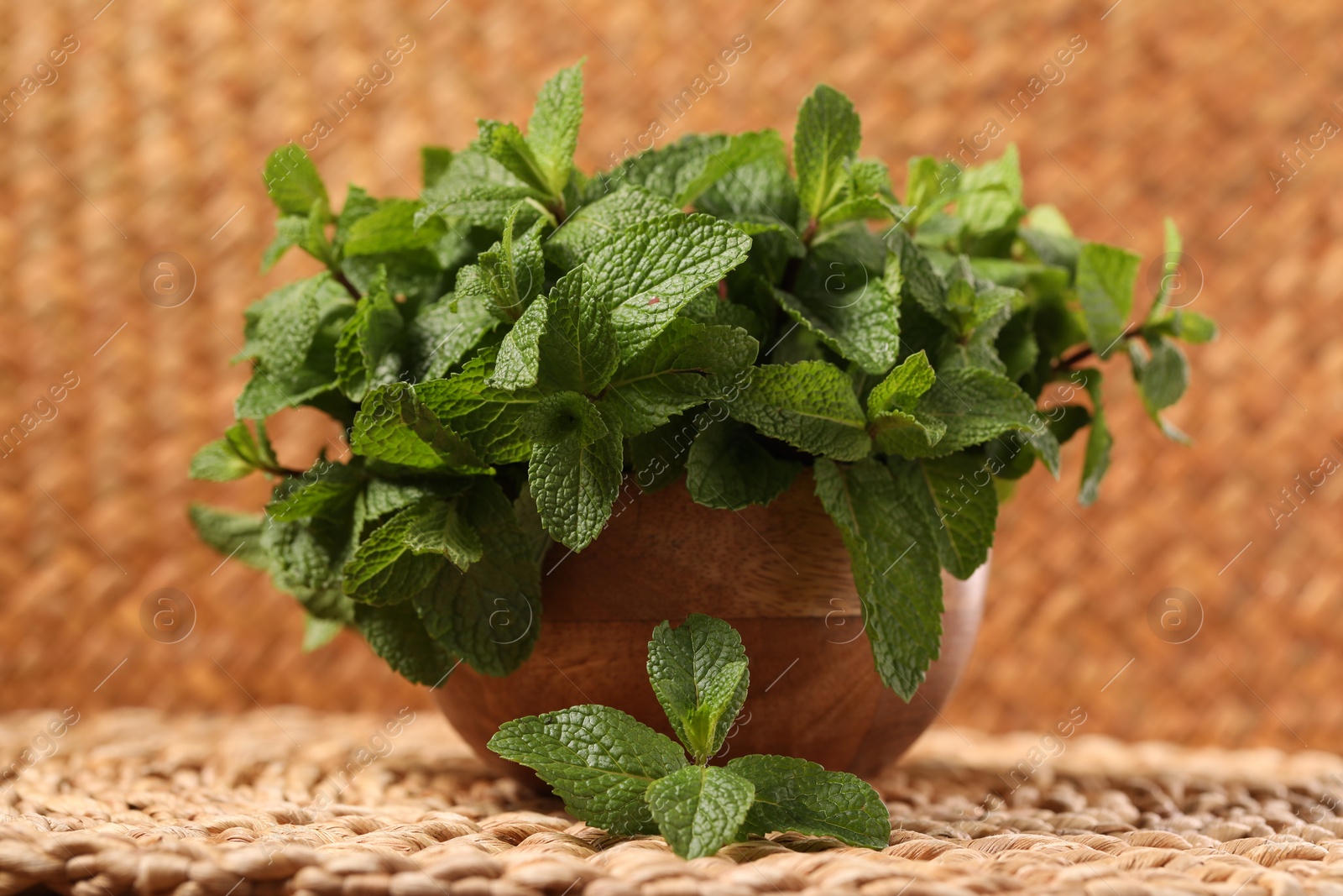 Photo of Bowl with fresh green mint leaves on wicker mat, closeup