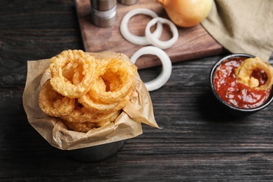 Photo of Dishware with homemade crunchy fried onion rings and tomato sauce on wooden table