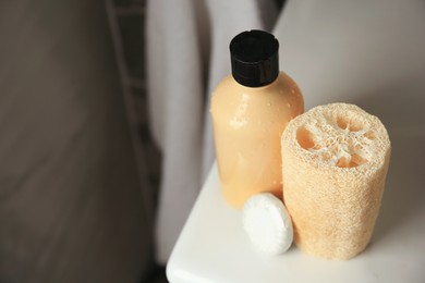 Natural loofah sponge and shower gel bottle on washbasin in bathroom, space for text