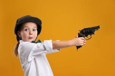 Photo of Cute little detective with revolver on yellow background