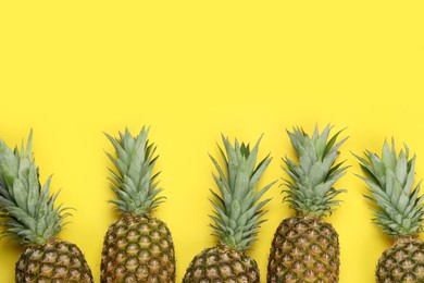 Whole ripe pineapples on yellow background, flat lay. Space for text