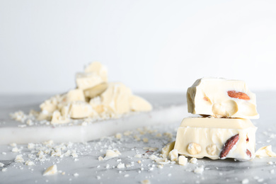 Photo of Pieces of tasty white chocolate with nuts on marble table, closeup. Space for text