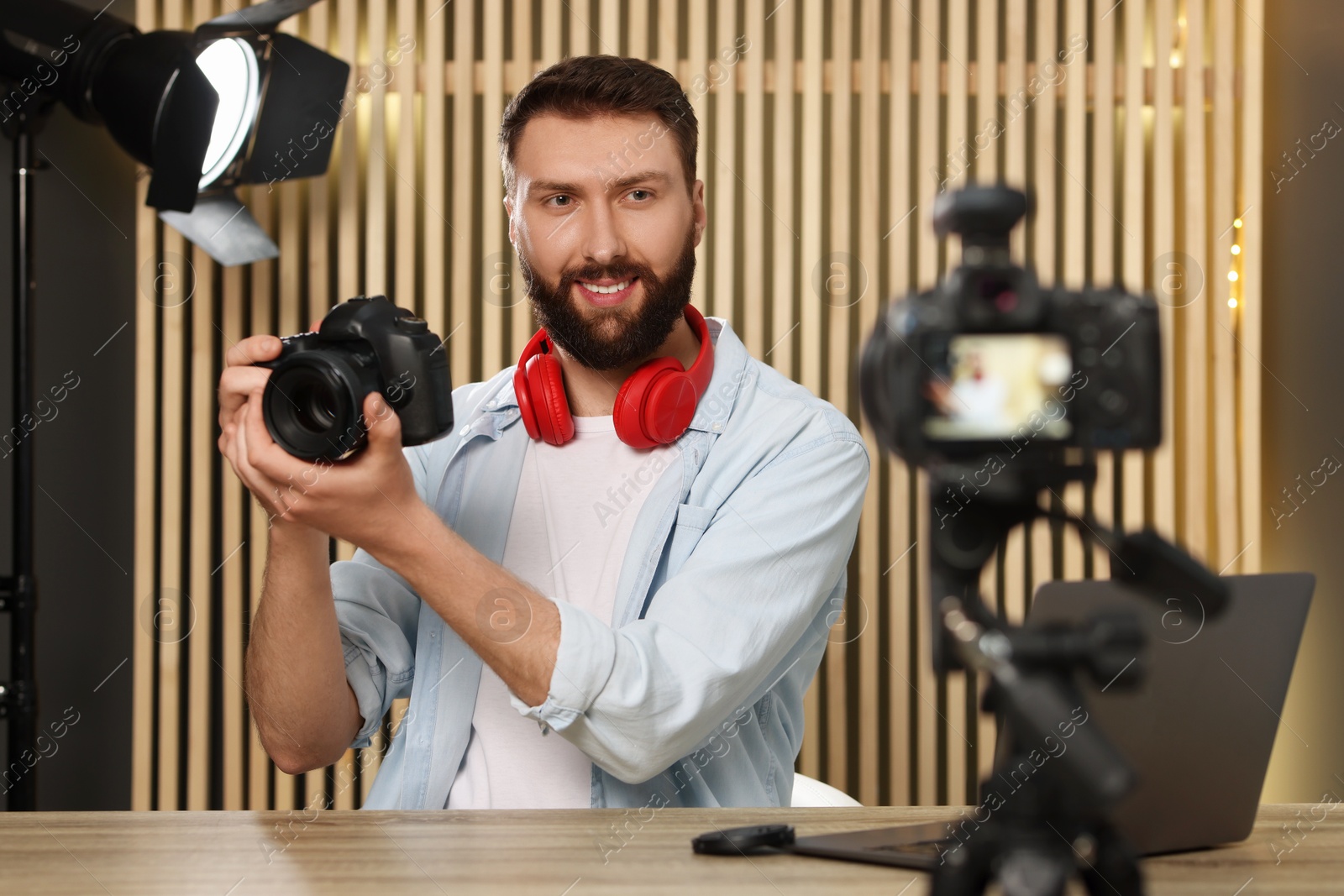 Photo of Smiling technology blogger with camera recording video review at home