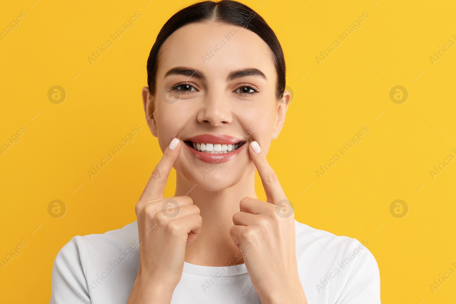 Photo of Beautiful woman showing her clean teeth and smiling on yellow background
