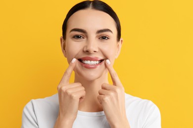 Beautiful woman showing her clean teeth and smiling on yellow background