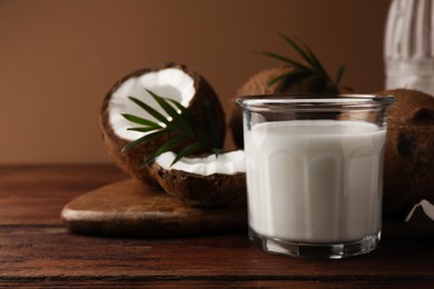 Glass of delicious vegan milk, coconut pieces and palm leaves on wooden table, space for text