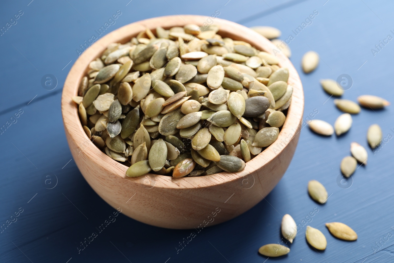 Photo of Bowl with peeled pumpkin seeds on blue wooden table, closeup