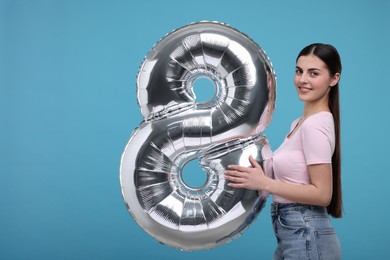 Photo of Happy Women's Day. Charming lady holding balloon in shape of number 8 on light blue background