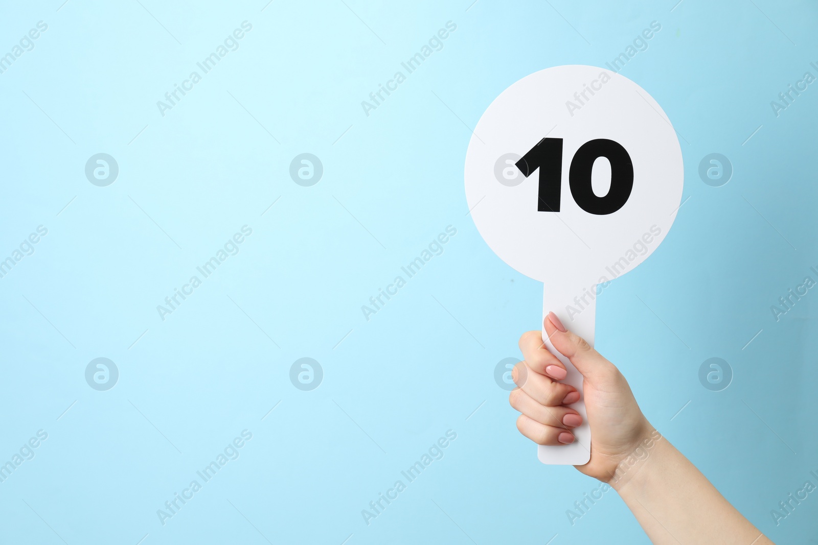 Photo of Woman holding auction paddle with number 10 on light blue background, closeup. Space for text