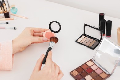 Photo of Woman with blusher and brush at dressing table indoors, closeup