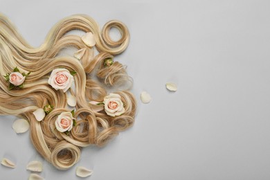 Photo of Lock of healthy blond hair with flowers on light grey background, flat lay. Space for text