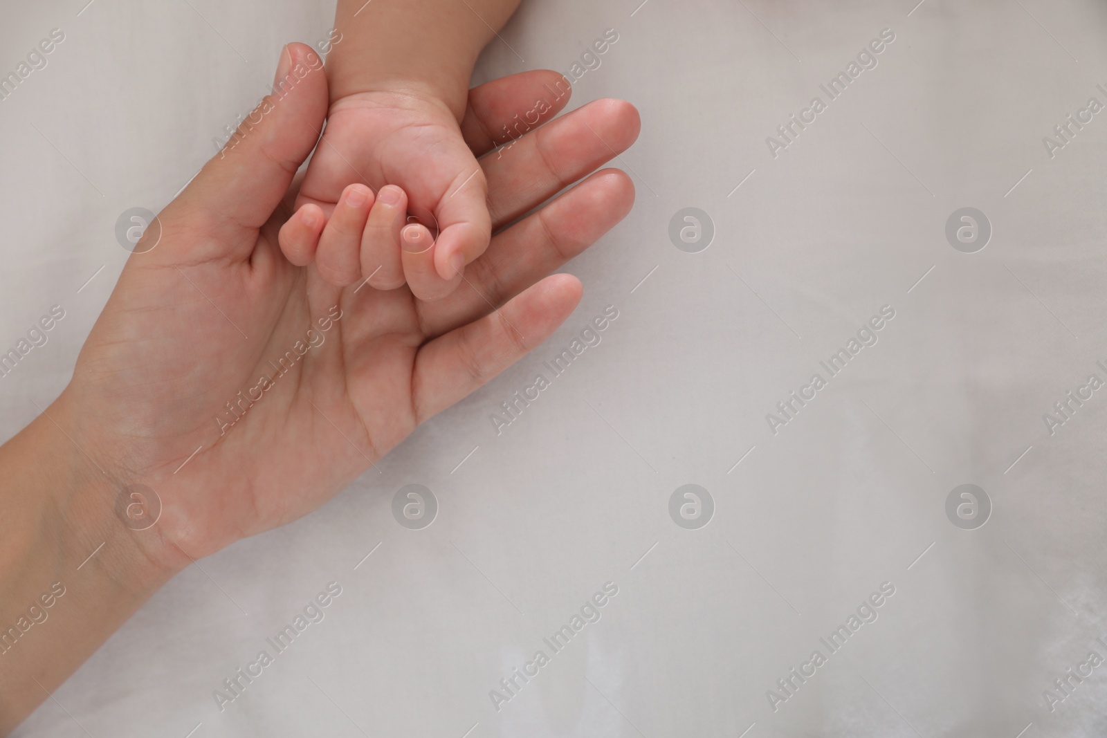 Photo of Mother with her baby on bed, closeup of hands. Space for text