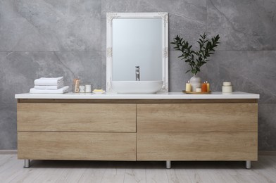 Beautiful plant in vase and burning candles near vessel sink and mirror on bathroom vanity