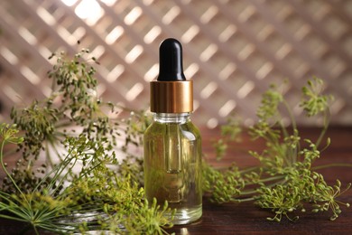 Photo of Bottle of essential oil and fresh dill on wooden table, closeup