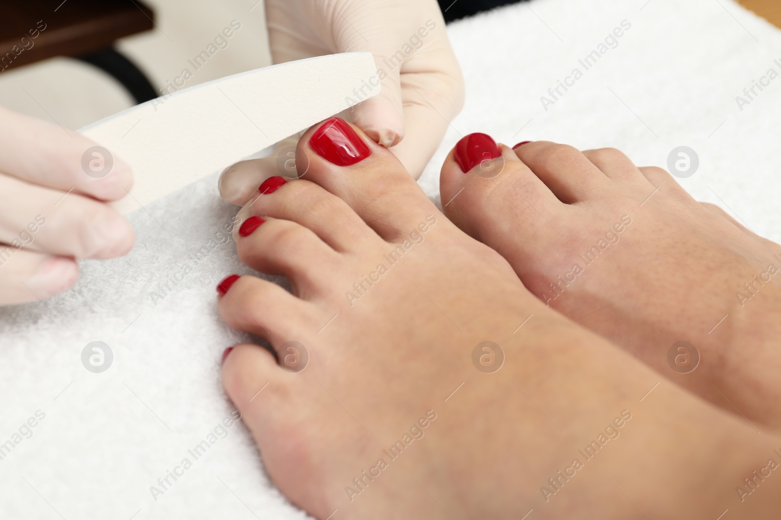 Photo of Pedicurist filing client`s toenails in beauty salon, closeup