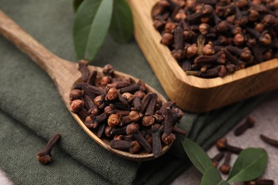 Photo of Bowl with aromatic cloves, spoon and green leaves on table, closeup