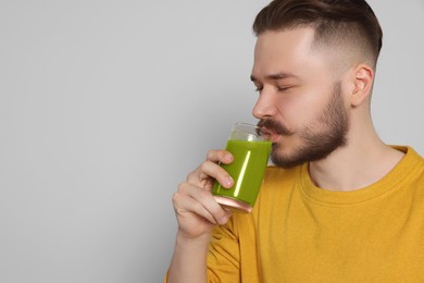 Photo of Handsome young man drinking juice on light grey background. Space for text