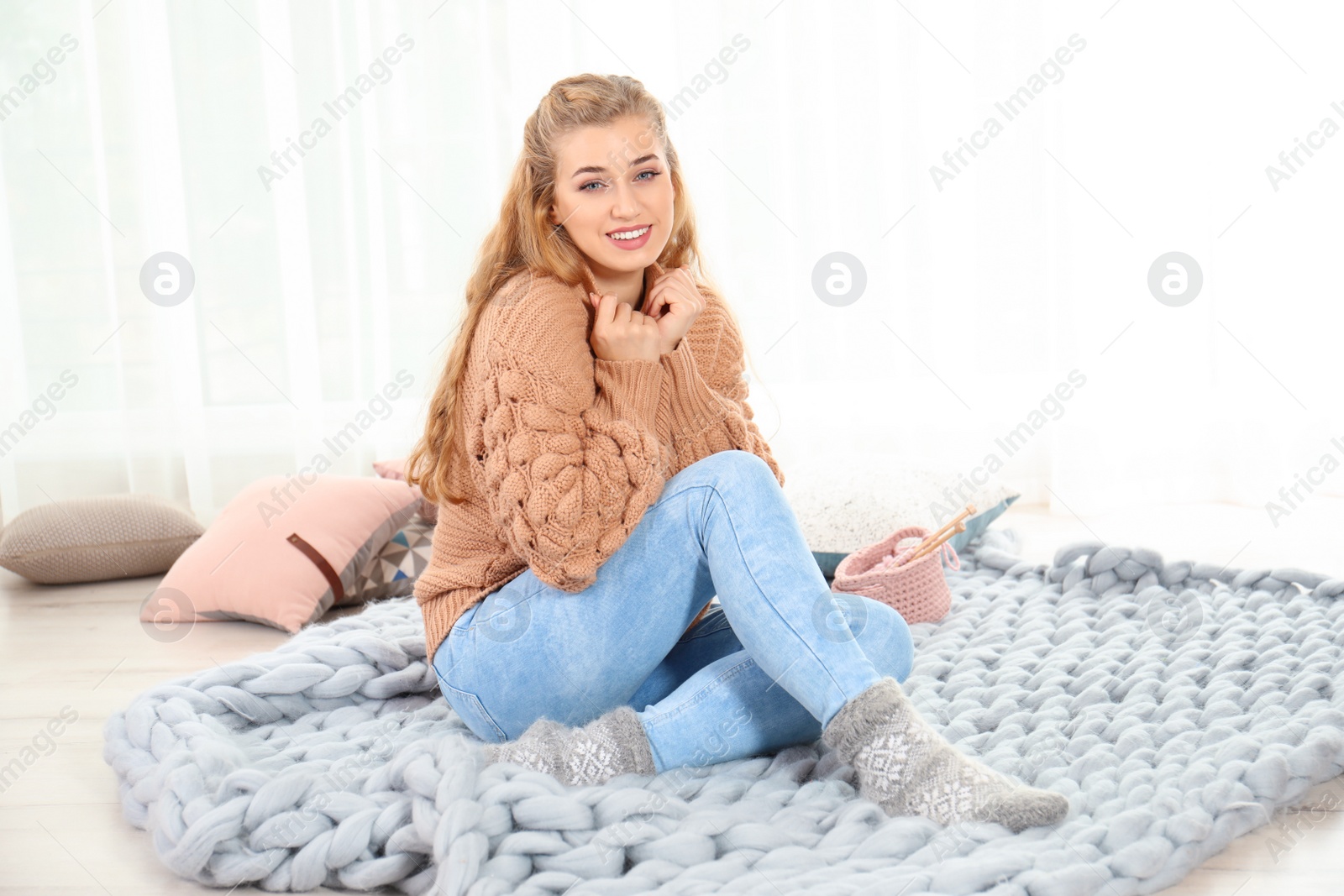 Photo of Attractive young woman in cozy warm sweater sitting on floor at home