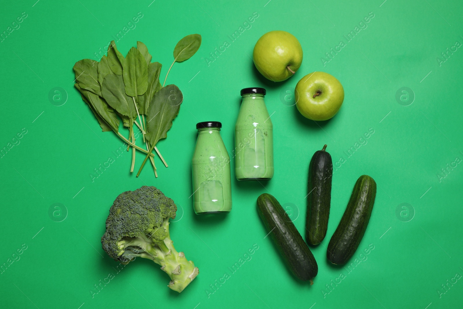 Photo of Bottles of delicious smoothie and ingredients on green background, flat lay