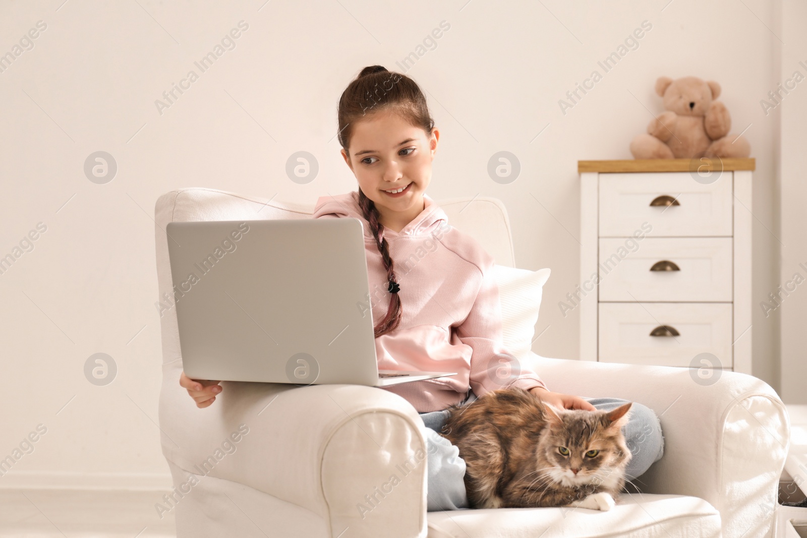 Photo of Cute little girl with laptop and cat in armchair at home. First pet