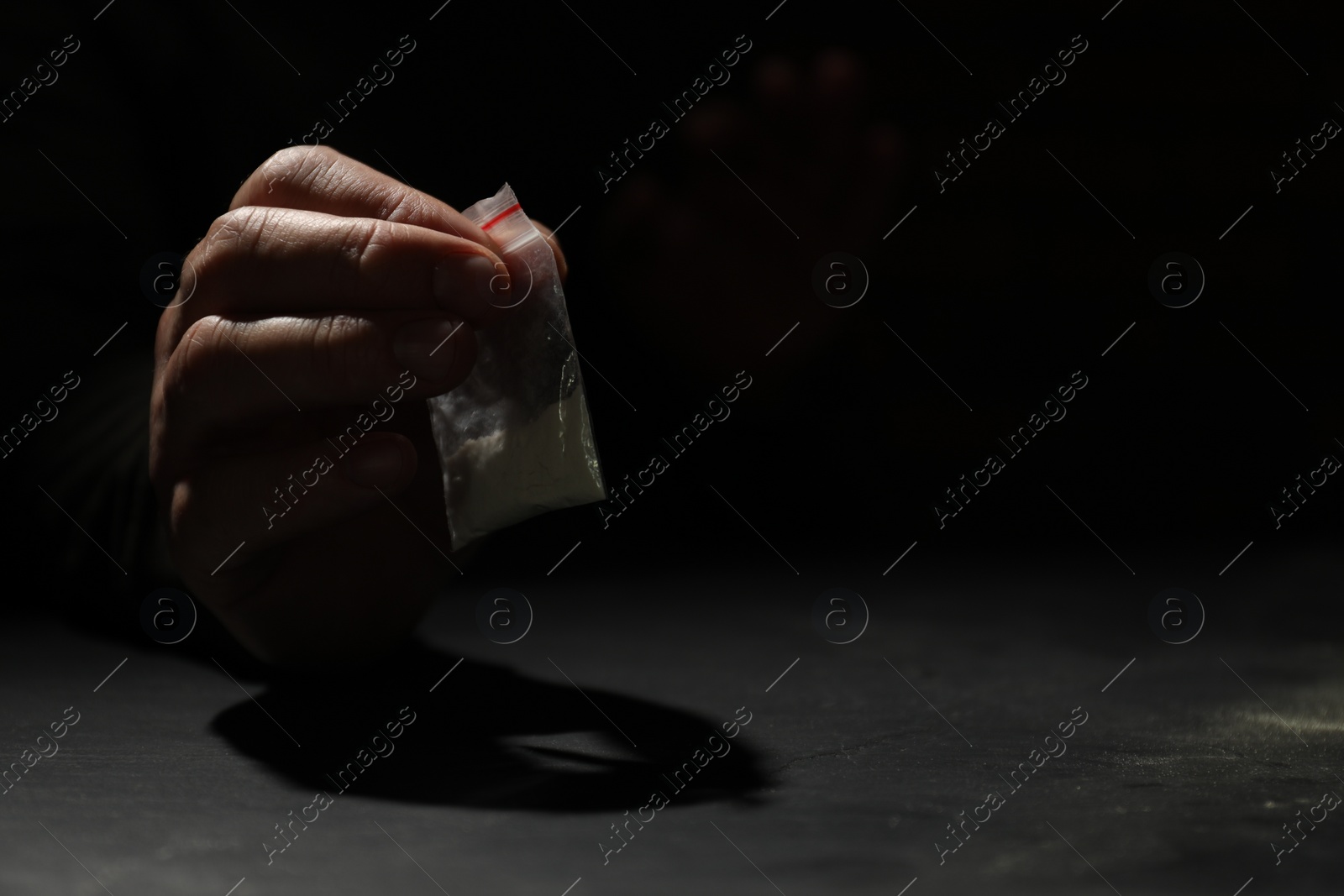 Photo of Addicted man with plastic bag of hard drug at grey table, closeup. Space for text