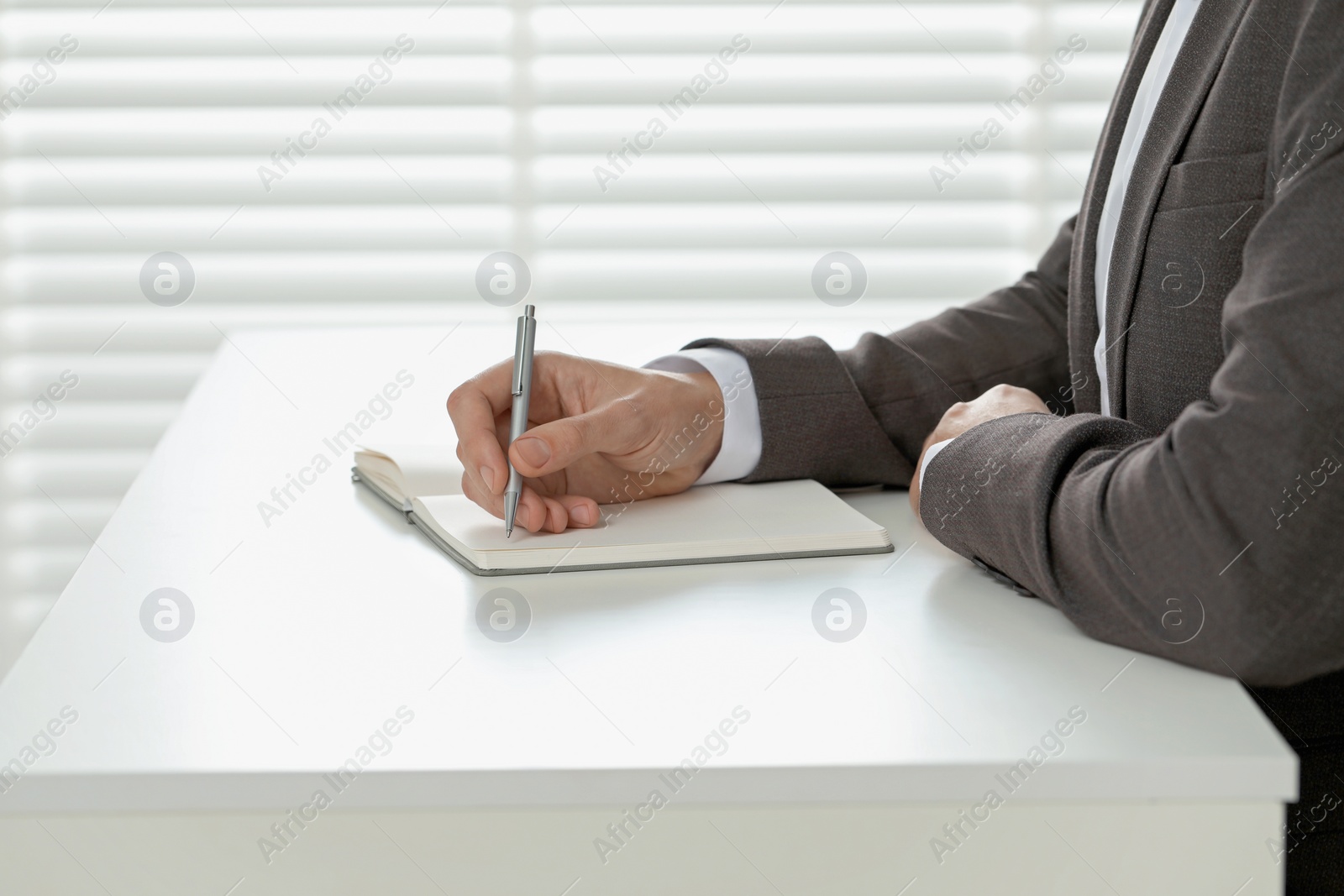 Photo of Man writing in notebook at white table indoors, closeup