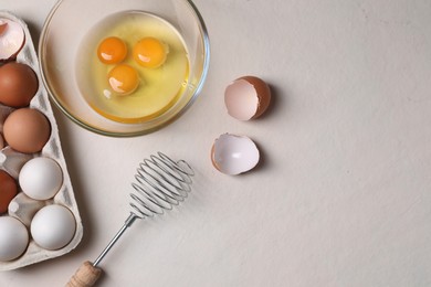 Photo of Metal whisk, raw eggs and shells on light table, flat lay. Space for text